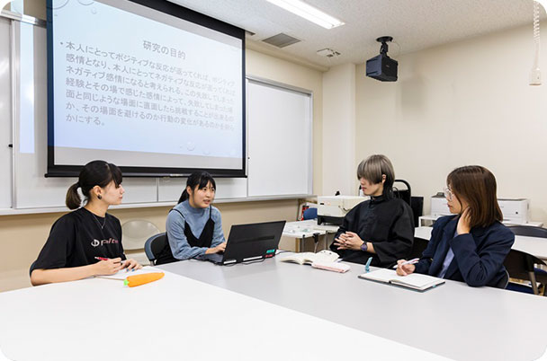 写真:学生たちが話し合いをしている様子。背後のロールスクリーンには「研究の目的」という内容の文章が映し出されている