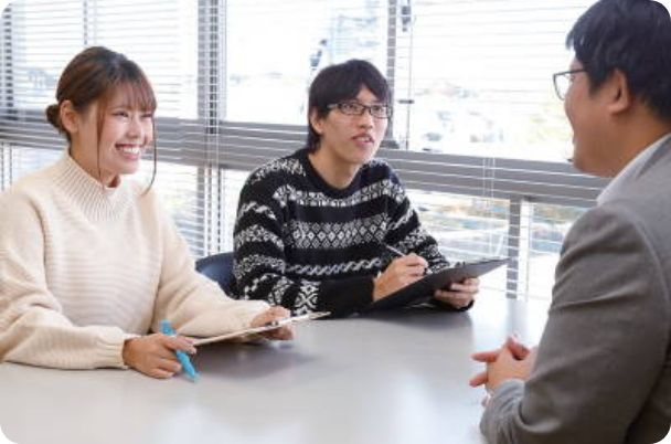 写真:スーツを着た男性と向かい合い、カウンセリングにチャレンジしているふたりの学生